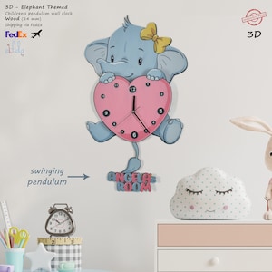 May include: A 3D wooden pendulum clock featuring a blue elephant holding a pink heart-shaped clock face. The clock face has black hands and black numbers. The elephant has a yellow bow on its head. The clock is labelled "Angela's Room" in pink and blue letters. The clock is 24 mm thick.
