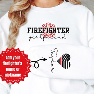 May include: White sweatshirt with the text "FIREFIGHTER girlfriend" and a red firefighter emblem.  There is a red star with the text "Add your firefighter's name or nickname" and an arrow pointing to the bottom right corner of the sweatshirt where the text "Taylor" is written in cursive with a red and black heart with stars.