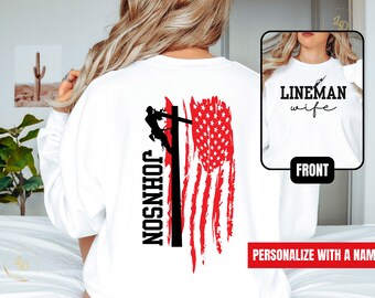 May include: White long-sleeve shirt with a distressed American flag design and a silhouette of a lineman climbing a utility pole. The text "JOHNSON" is printed vertically on the pole. The front of the shirt has the text "LINEMAN wife" printed on it.