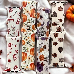 May include: Four different Apple Watch bands with Halloween-themed designs. The bands are white with various patterns, including pumpkins, skulls, and bloody handprints.