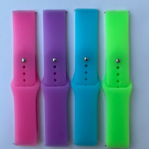 May include: Four silicone watch bands in pink, purple, blue, and green. The bands are all the same size and have a silver buckle.