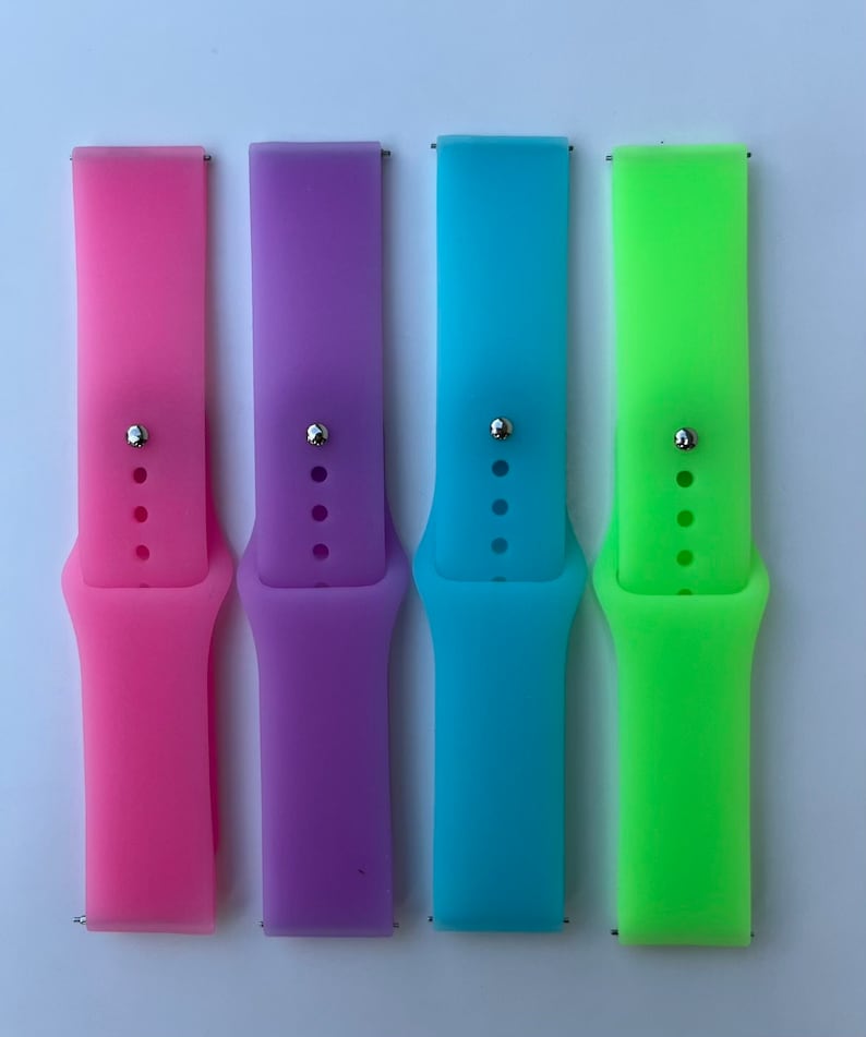 May include: Four silicone watch bands in pink, purple, blue, and green. The bands are all the same size and have a silver buckle.