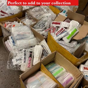 May include: A variety of watch bands in different colors and patterns, including painted, engraved, and blank bands. The bands are packaged in individual plastic bags and are arranged in boxes. The text "Mystery bands variety from Painted, engraved and blank bands Perfect to add to your collection" is visible at the top of the image.