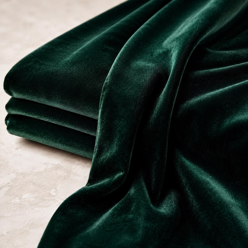 a close-up view of a pile of dark green velvet fabric, with its smooth and shiny texture visible.