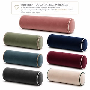 May include: Seven cylindrical velvet bolster pillows in various colors including dusty rose, olive green, navy blue, teal, burgundy, charcoal gray, and cream, each featuring contrasting piping. Text reads: DIFFERENT COLOR PIPING AVAILABLE.