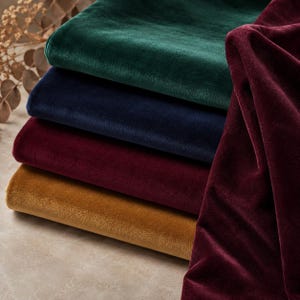 A stack of five velvet fabric swatches in various colors, including green, blue, red, maroon, and gold.