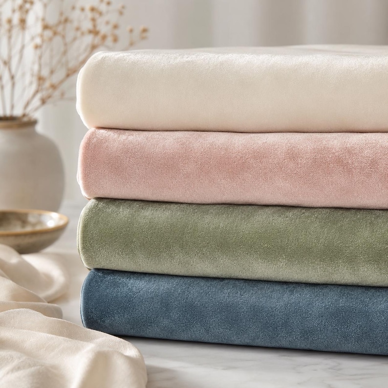 A stack of four fabric swatches in various colors, including white, pink, green, and blue, arranged on a white surface.