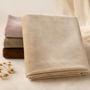 a stack of three folded beige fabric pieces, with a small decorative item, possibly a flower, placed to the left of the stack.