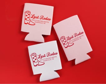 May include: Three white and pink can coolers with a red cowboy boot and heart design. The text "Last Rodeo" and "Kelly's Bachelorette Nashville, TN" are printed on the coolers. The background is red.