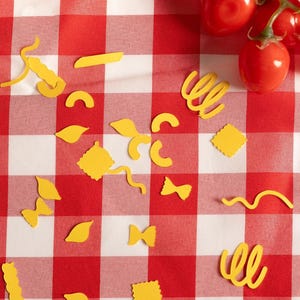 Puede incluir: Un mantel a cuadros rojos y blancos con formas de pasta amarillas dispersas y un racimo de tomates cherry rojos frescos. Las formas de pasta incluyen lazos, espirales y cuadrados.