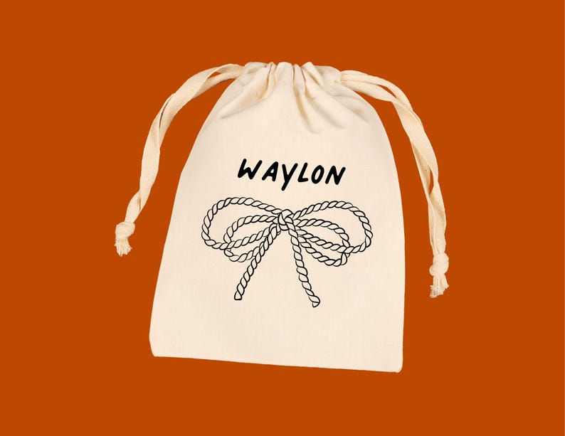 Puede incluir: Una bolsa con cord&oacute;n de color crema con el nombre "WAYLON" en escritura negra sobre un dise&ntilde;o de lazo de cuerda negra. La bolsa tiene cordones de color crema sobre un fondo naranja.
