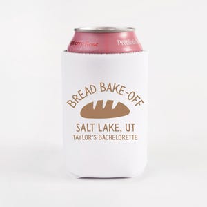 May include: White can cooler with the text "BREAD BAKE-OFF" and a bread loaf graphic. Below the text is "SALT LAKE, UT" and "TAYLOR'S BACHELORETTE". A pink can of "berry Rose" is inside the cooler.