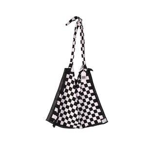 May include: A black and white checkered tote bag with a long, knotted strap. The bag has a triangular shape and a small tag attached. The checkered pattern is consistent throughout the bag and strap.