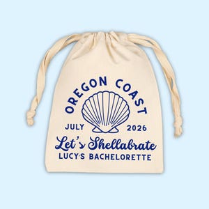 May include: A cream-colored drawstring bag with blue text and a seashell graphic. The text reads "Oregon Coast July 2026 Let's Shellabrate Lucy's Bachelorette."