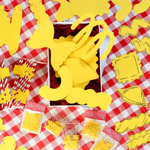 May include: A collection of yellow pasta-themed decorations and party supplies on a red and white checkered tablecloth. Includes various pasta shapes, paper straws, and small bags labeled "Pasta Party."