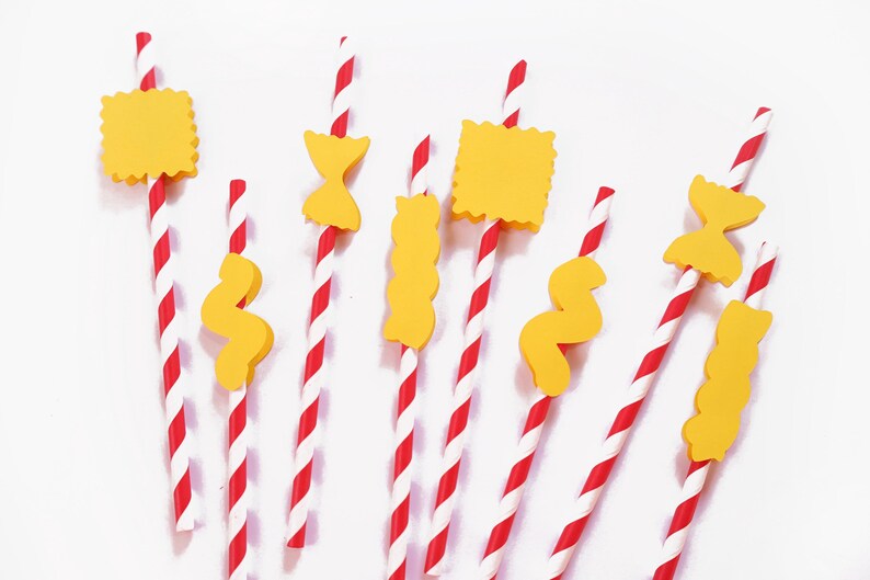 May include: A collection of red and white striped paper straws, each adorned with a yellow pasta-shaped decoration. The pasta shapes include bow ties, wavy ribbons, and squares. The straws are arranged against a white background.