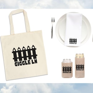 Puede incluir: Colecci&oacute;n de art&iacute;culos con un dise&ntilde;o de valla negra y el texto "GIGGLE LN" en una bolsa de mano color crema, una servilleta blanca sobre un plato y dos enfriadores de latas. Un tenedor y un cuchillo est&aacute;n a cada lado del plato.