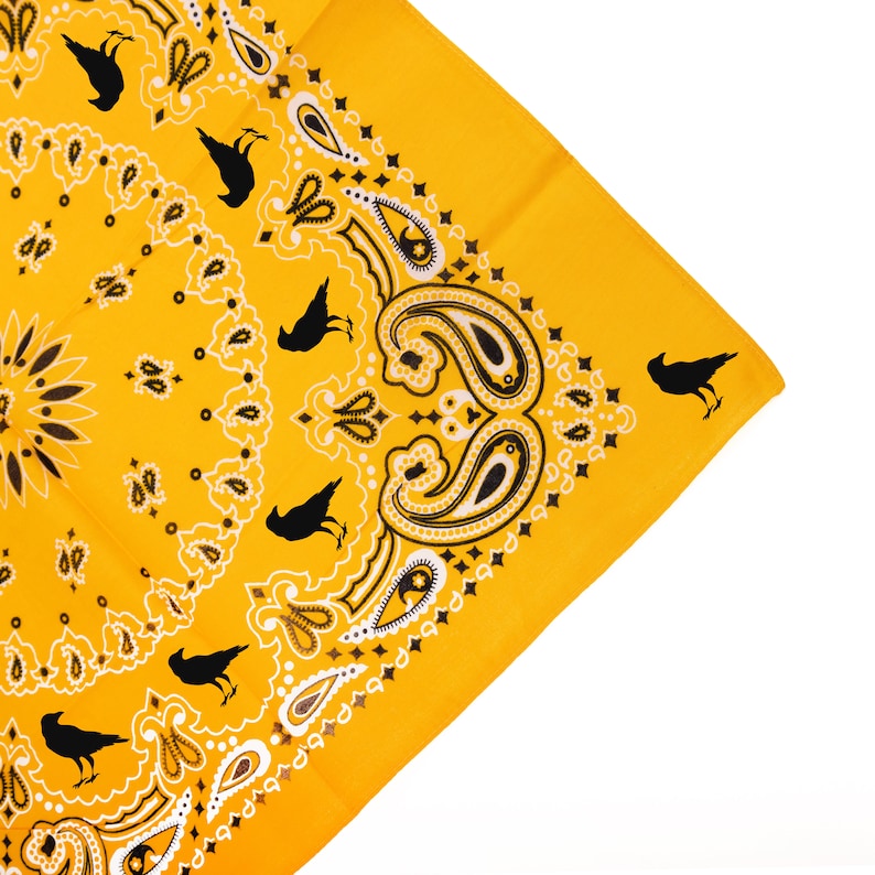 May include: A yellow bandana with a paisley pattern and black crow silhouettes. The bandana has a white border.
