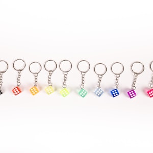 May include: A set of 12 colorful dice keychains. The dice are translucent and feature white dots. The keychains are attached to silver rings and chains.