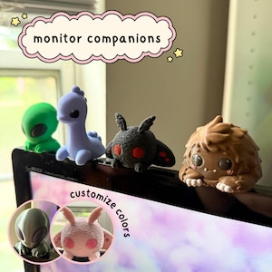 May include: A set of small figurines labelled monitor companions, including a green alien, a light purple long-necked creature, a black moth with red eyes, and a brown furry creature. Two circular insets show a metallic alien and a pink moth.