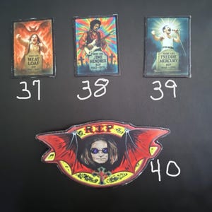 May include: A collection of four patches featuring rock and roll legends. The patches include images of Meat Loaf, Jimi Hendrix, Freddie Mercury, and Ozzy Osbourne. Each patch has a unique design and color scheme, with the names and dates of the musicians.
