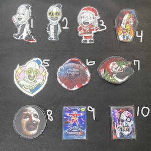 May include: Ten iron-on patches featuring various horror movie characters, including clowns, a Santa Claus, and a creature with a bloody face. The patches are all different sizes and shapes, and some have text on them, such as "Terrifier".