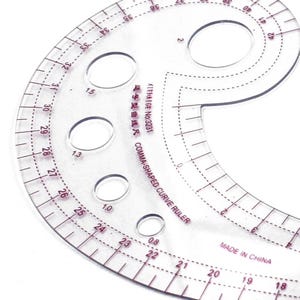 May include: A clear, comma-shaped curve ruler with red markings and several circular cutouts. The ruler has measurements in inches and the text "COMMA-SHAPED CURVE RULER" and "MADE IN CHINA" is visible.