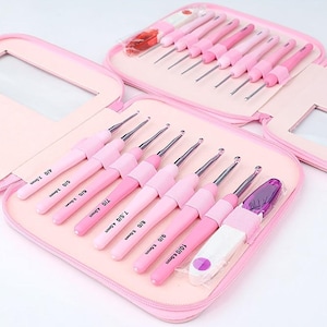 Puede incluir: Un juego de ganchillos rosas en un estuche con cremallera. El juego incluye múltiples ganchillos de diferentes tamaños, de 2,5 mm a 6,0 mm, cada uno con un mango rosa. El estuche también es rosa y tiene un bolsillo transparente.