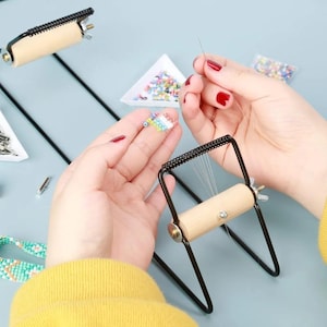 May include: A black metal bead loom with a wooden handle and a spring-loaded mechanism. The loom is used to create beaded bracelets and necklaces.