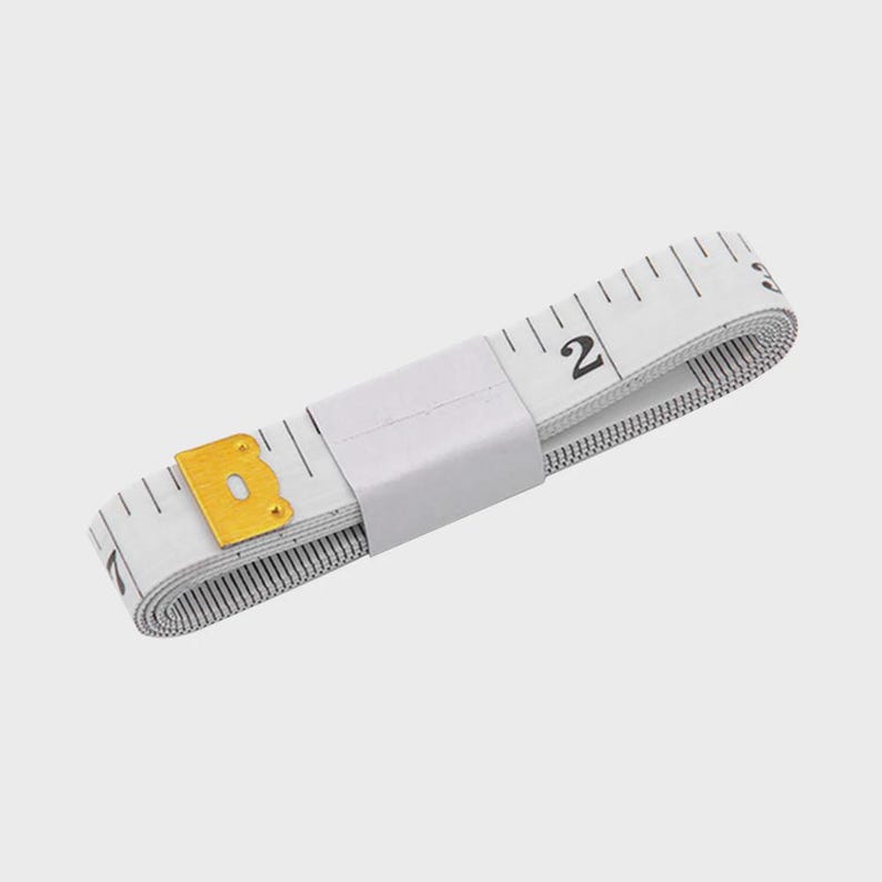 May include: A white and black measuring tape with black markings and a gold-colored metal end piece. The tape is rolled up and held together with a white band. The tape measures in inches.
