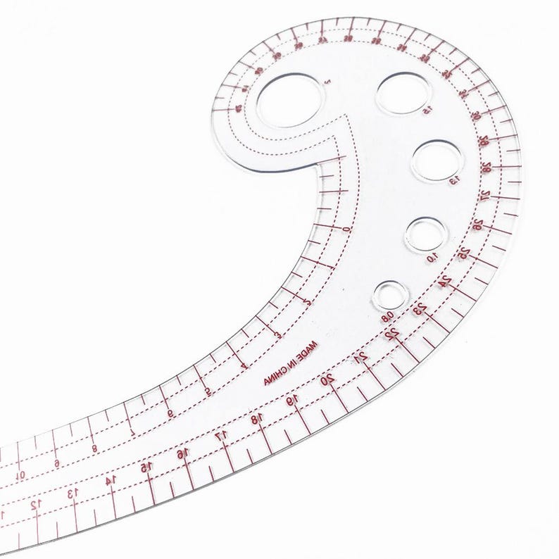 May include: A clear, plastic French curve ruler with red markings and measurements. The ruler has a curved shape with multiple holes and is marked with numbers and lines for precise measurements. The text "MADE IN CHINA" is visible.