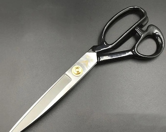 May include: A pair of large, professional-grade scissors with black handles and silver blades. The blades are sharp and pointed, with a gold-colored rivet in the center. The scissors are designed for cutting fabric or other materials.