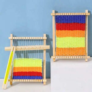 May include: Two wooden weaving looms with colorful yarn. The yarn is woven in horizontal stripes of blue, red, orange, yellow, and orange. The looms are made of light-colored wood and have a rectangular frame.