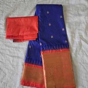 May include: A blue saree with a gold and red border and a matching red blouse piece. The saree has a grid pattern with gold floral accents. The border features intricate gold designs. The text "Galaxy S24" is visible in the bottom left corner.