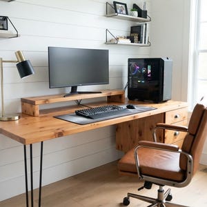 Peut inclure: Un bureau en bois avec des pieds en épingle en métal noir, un support d'écran en bois assorti, un écran d'ordinateur noir, un clavier noir, une souris noire, une lampe de bureau en laiton et noir, et une chaise de bureau en cuir marron.