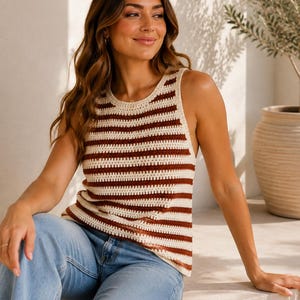 Peut inclure: Un débardeur en crochet sans manches avec des rayures horizontales alternant entre le crème et le marron foncé. Le vêtement présente une encolure ronde et un ourlet droit, associé à un jean en denim bleu clair au design classique à cinq poches.