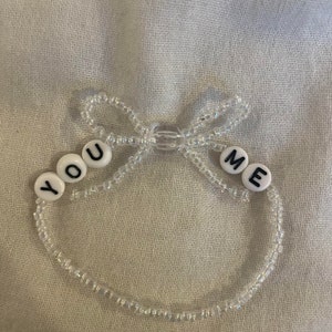 May include: A white beaded bracelet with the words "YOU ME" spelled out in black letters.
