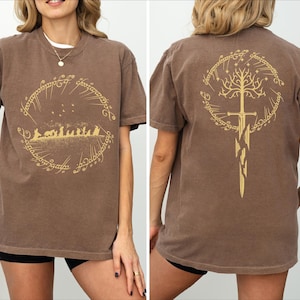 a woman wearing a brown t-shirt with a graphic design featuring a golden tree and a golden sword on the back.