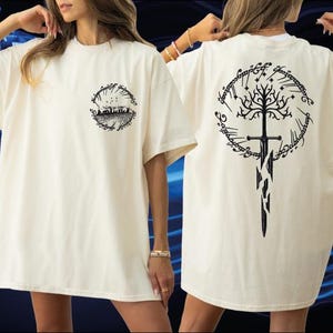 A woman wearing a white t-shirt with a black graphic design on the back, including a tree and a sword.