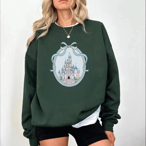 A woman wearing a green sweatshirt with a castle graphic on it.