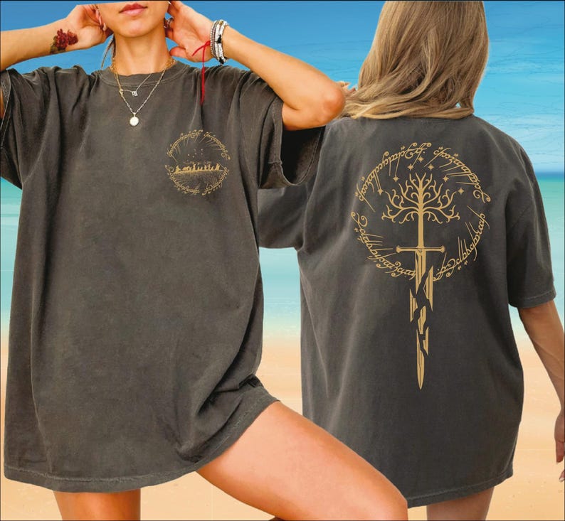 A woman wearing a gray t-shirt with a tree design on the back, posing on a beach with a blue sky and ocean in the background.
