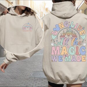A person wearing a beige hoodie with a colorful graphic design on the back, which appears to be a Disney-themed design.