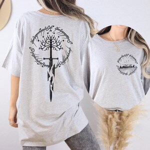 a person wearing a grey t-shirt with a graphic design on the back. The design includes a tree with a sword and a ring, which are common symbols associated with the Lord of the Rings series.