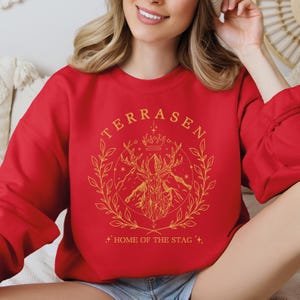 a woman sitting on a bed wearing a red sweatshirt