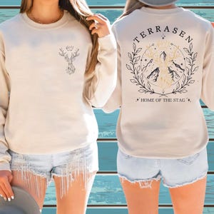 A woman wearing a white sweater with a graphic design on the back and denim shorts.