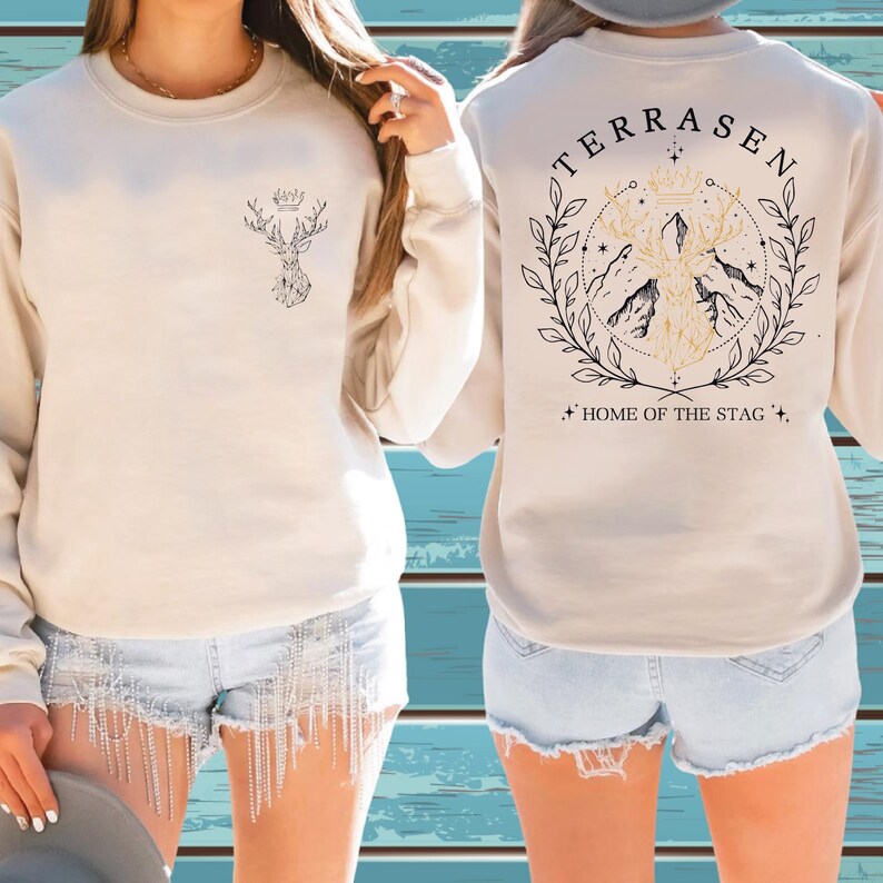 A woman wearing a white sweater with a graphic design on the back and denim shorts.