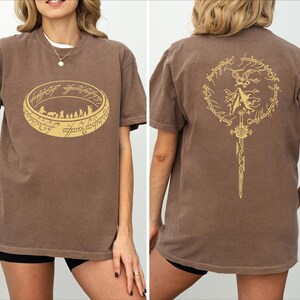 a woman wearing a brown t-shirt with a graphic design on the front and back.