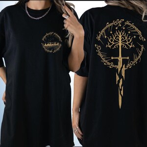 two black t-shirts with gold designs on the back. The design on the back of the t-shirt features a tree with a sword, and the text "The Lord of the Rings" is visible.