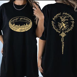 two black t-shirts with gold designs on the back. The design on the left features a circular emblem with a silhouette of a group of people, while the design on the right depicts a winged figure with a sword.