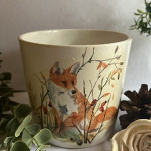 May include: White ceramic planter featuring a hand-painted design of a fox sitting in a woodland scene with autumn foliage and berries.